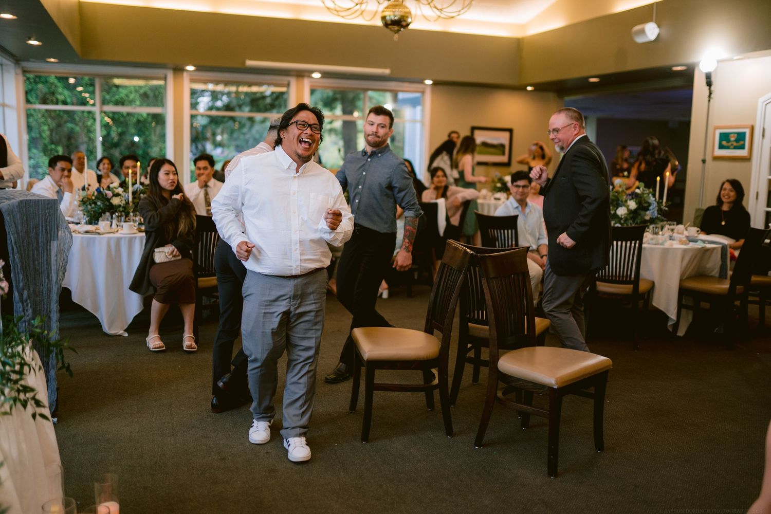 Wedding guests gather in an elegant dining room with carpeted floors and formal table settings.