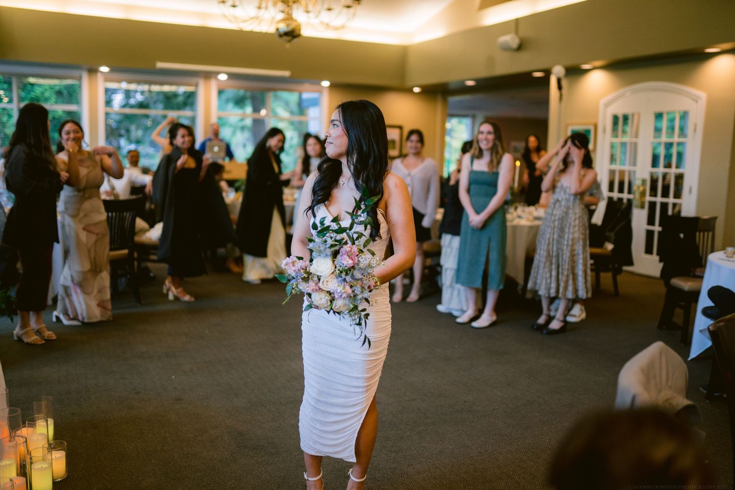 Wedding guests gather in a reception hall wearing formal attire and colorful dresses.