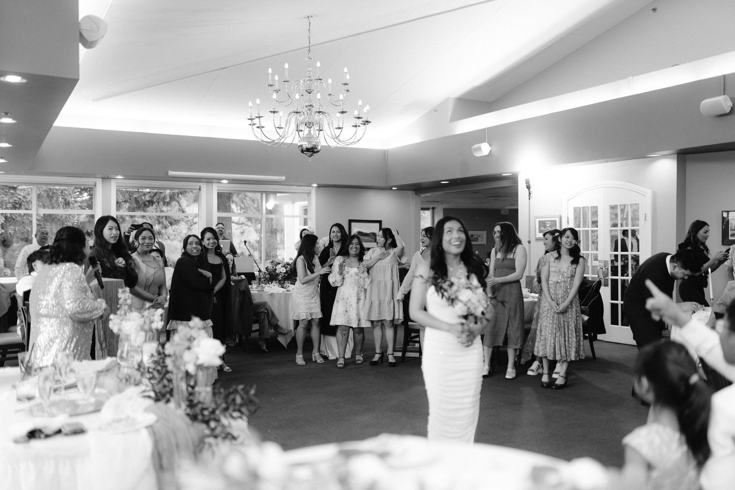 Black and white photo of wedding reception guests gathered in an elegant room with chandelier.