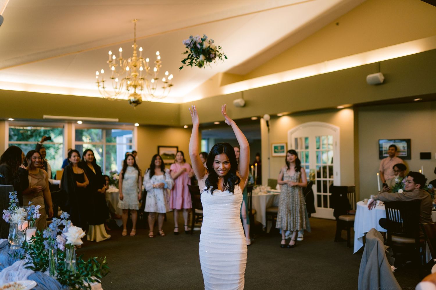A celebratory moment during a wedding reception with guests dancing under a chandelier.