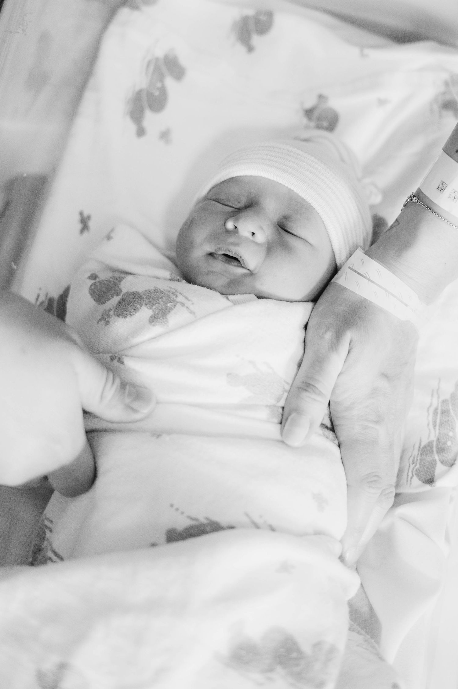 Peaceful newborn baby sleeps in white swaddle while being held against navy floral fabric.