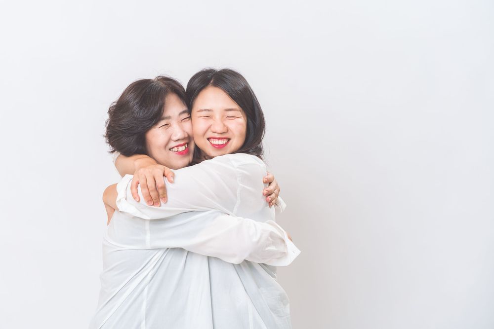 Two people in white shirts embracing and laughing against white background.