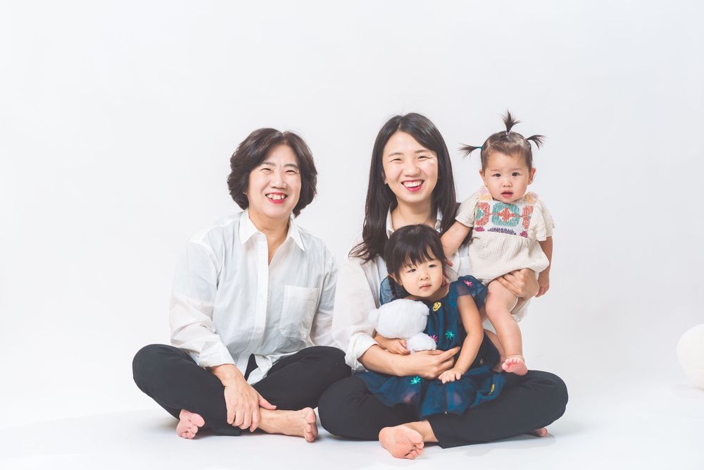 Casual family portrait with everyone sitting cross-legged on white background.