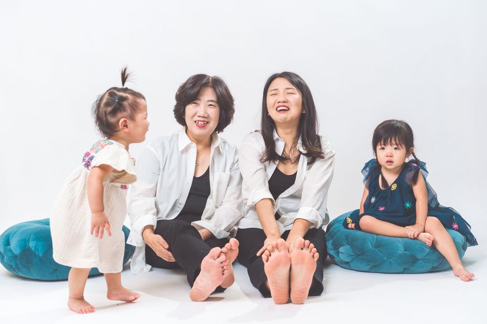 Family sitting together on blue cushions against white background showing playful expressions.