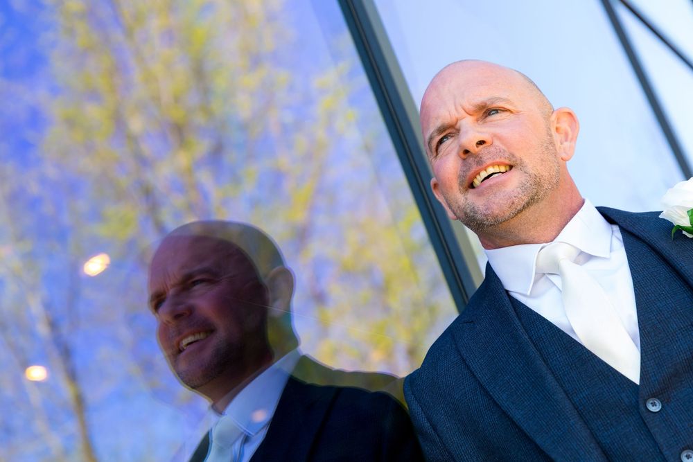 Groom Daniel smiling in front of reflective glass with trees behind at the Village Hotel, Portsmouth.
