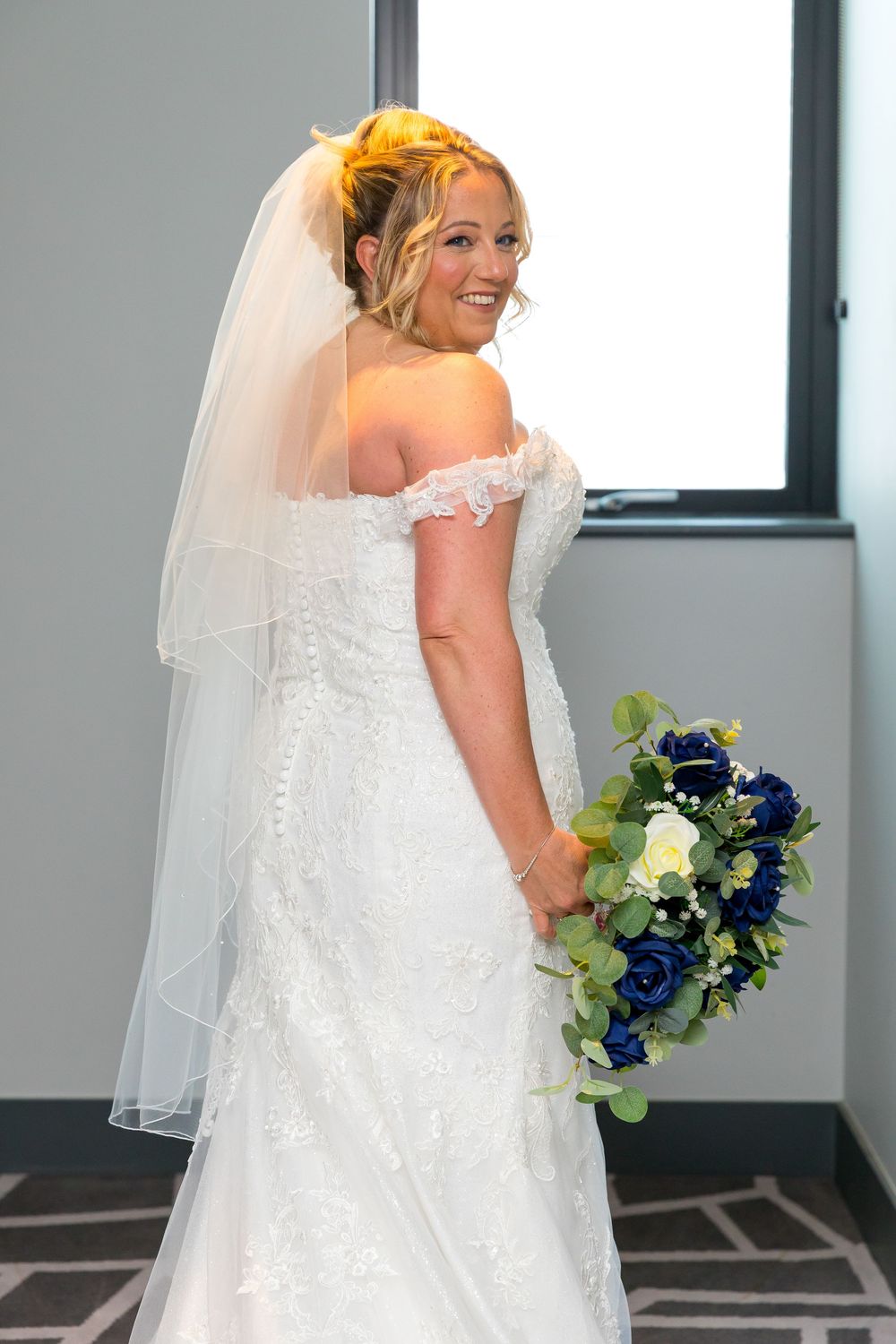 Bride Emma holding a blue and white bouquet, smiling in her lace wedding gown at the Village Hotel, Portsmouth.