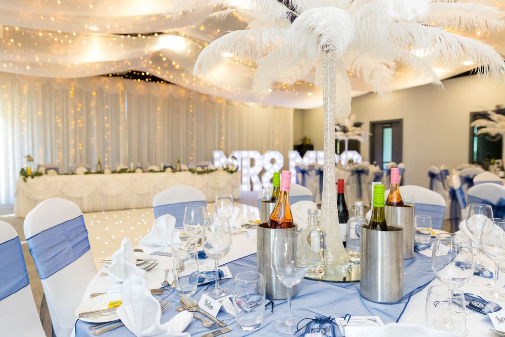 Elegant wedding reception setup with feather centrepieces, blue sashes, and twinkling ceiling lights.