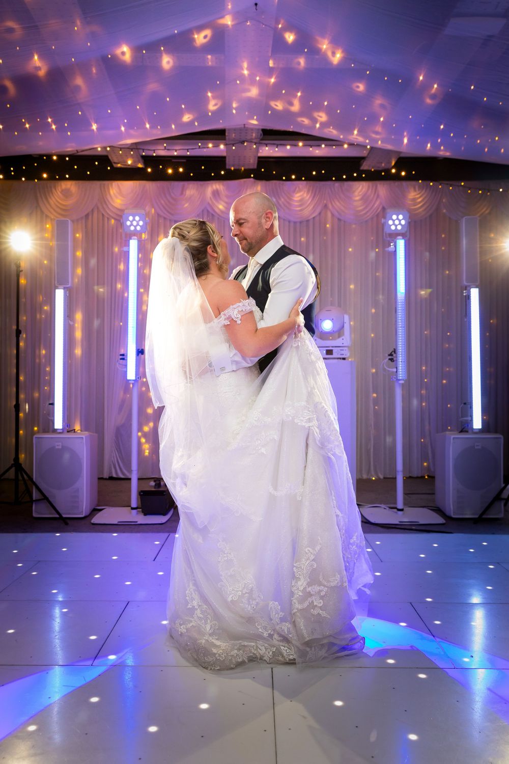 Bride and groom's romantic first dance on an LED dance floor under warm sparkling lights.