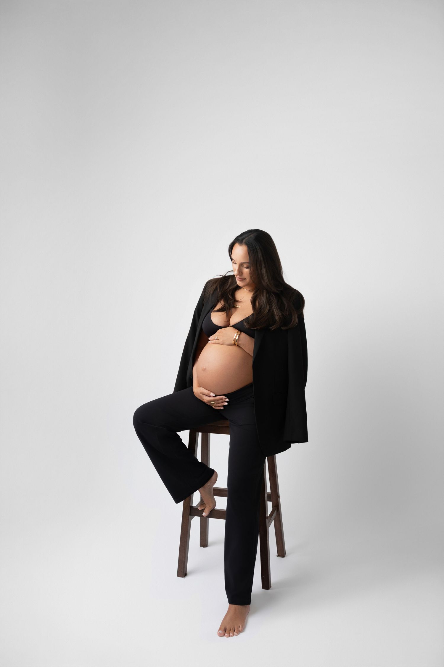Elegant maternity session featuring poses on wooden stool against white background.