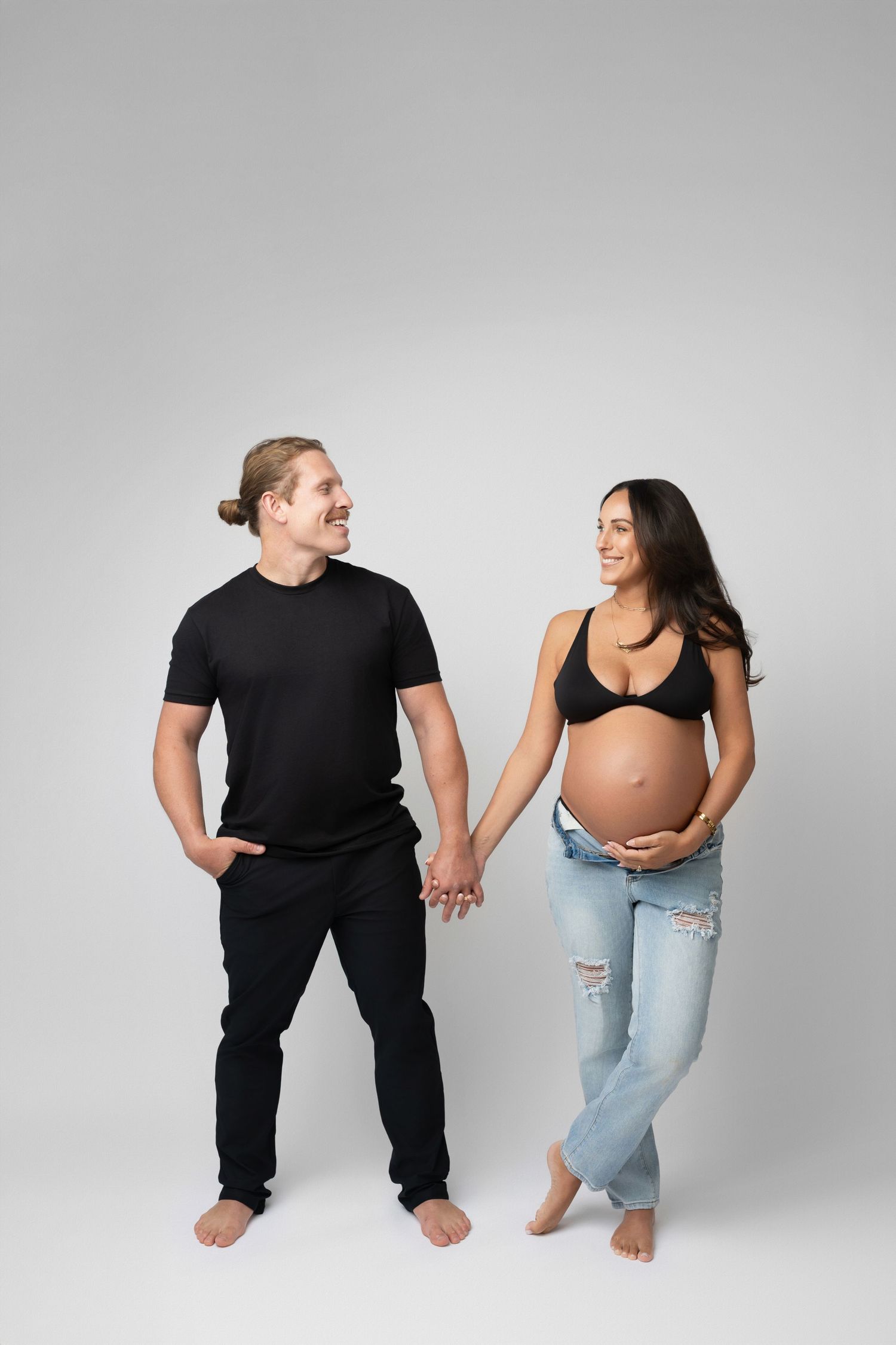 Couple shares intimate maternity moment in matching black outfits on white background.