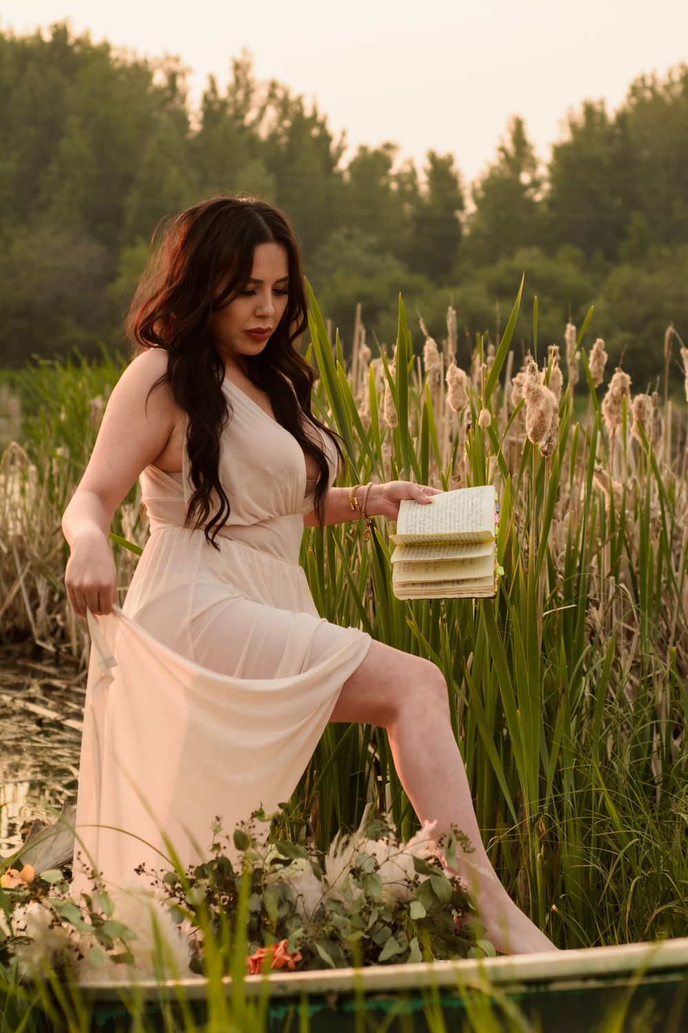 Dreamy photoshoot in white dress amongst tall cattails at golden hour beside a lake creates ethereal atmosphere.