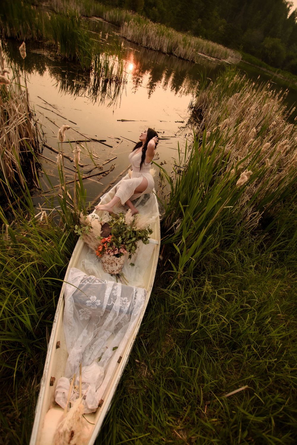 A white kayak with flowers rests in calm waters surrounded by reeds during a golden sunset.