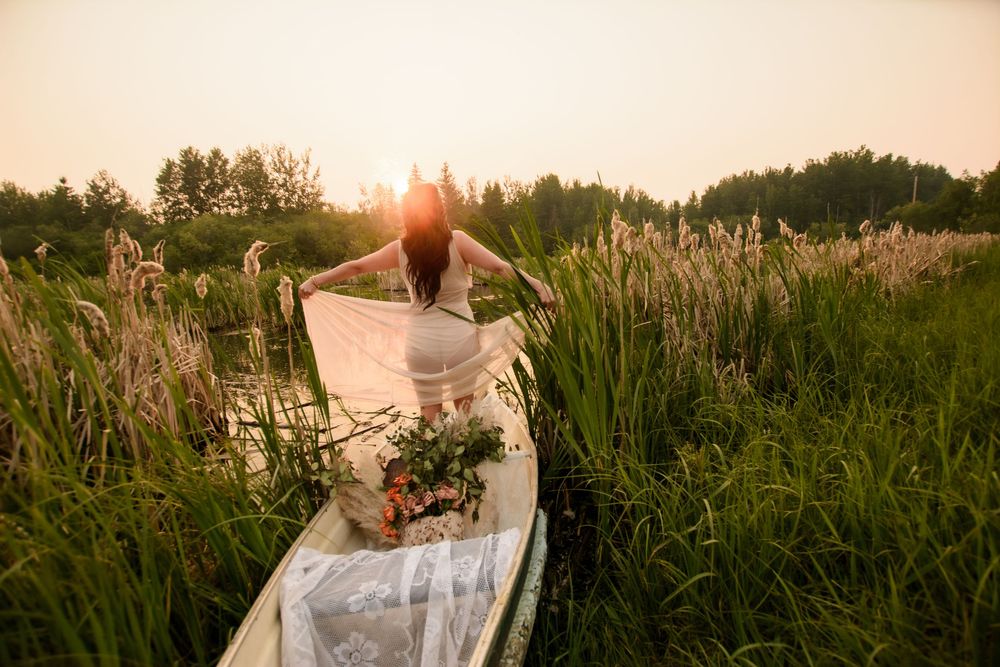 Scenic sunset view of someone in a white flowy dress sitting in tall grass meadow surrounded by golden light.