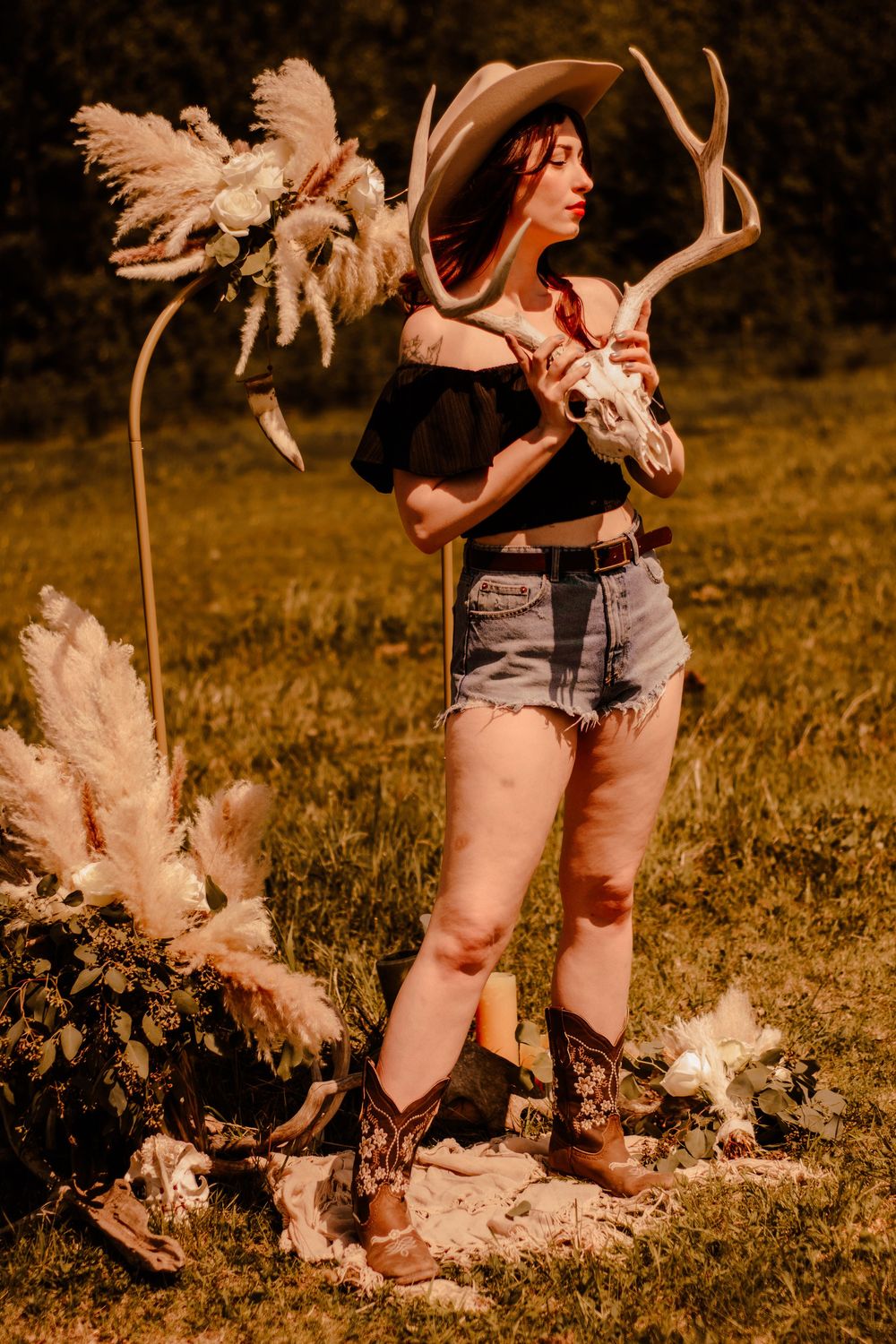 Woman in denim shorts holds dried pampas grass flowers in golden outdoor field.