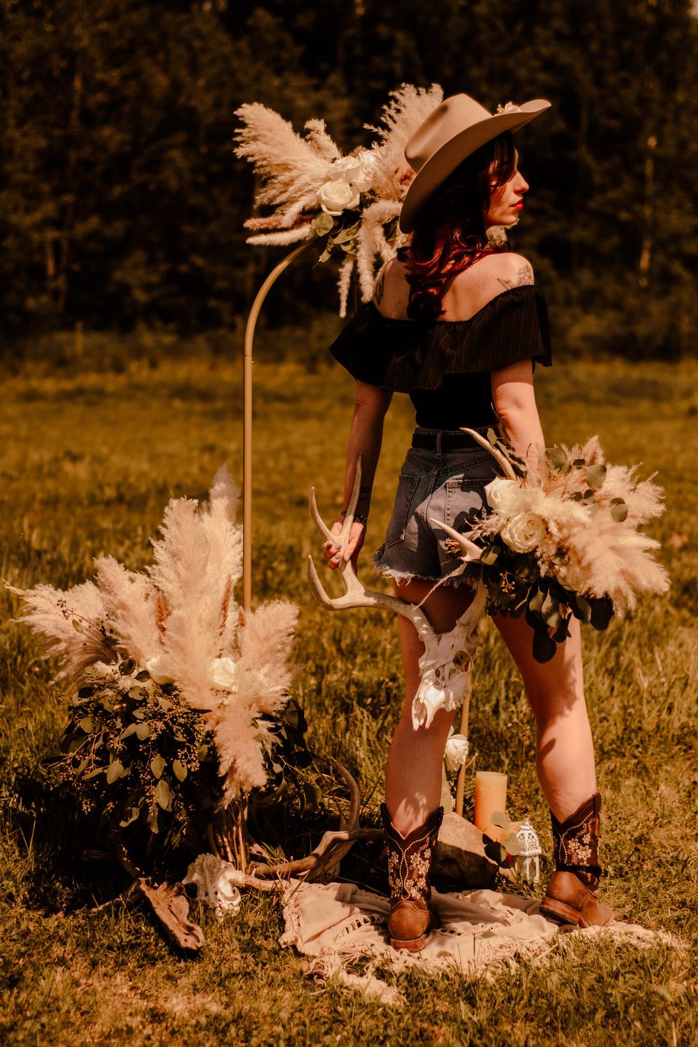 White pampas grass decorations set up in a field with boots and western accessories.