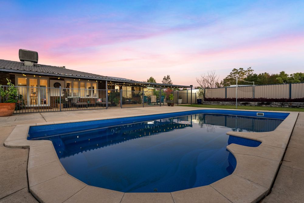 Modern motel with L-shaped swimming pool and patio area at dusk under pink and purple sunset sky.