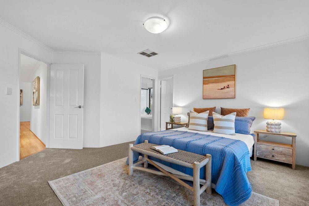 Modern bedroom with blue bedding, wooden bench, area rug and neutral decor showcasing bright natural lighting.