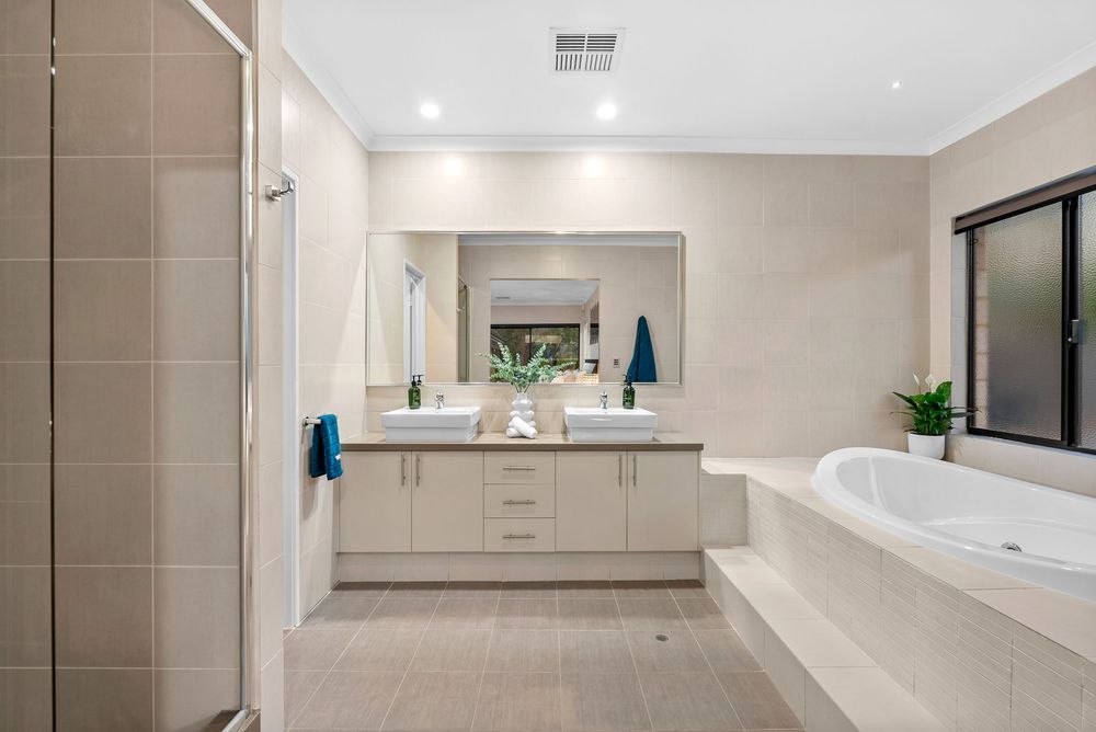 Modern master bathroom with beige tiles, white double vanity, step-up soaking tub and glass shower enclosure.
