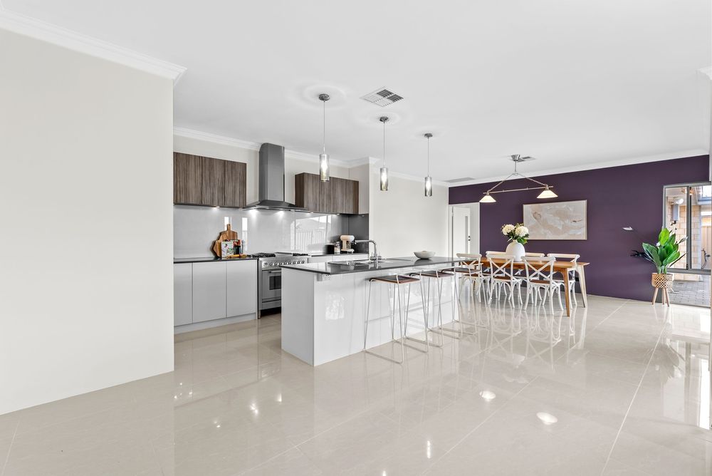 Modern white kitchen with purple accent wall features pendant lights, white countertops and a floating island with bar seating.
