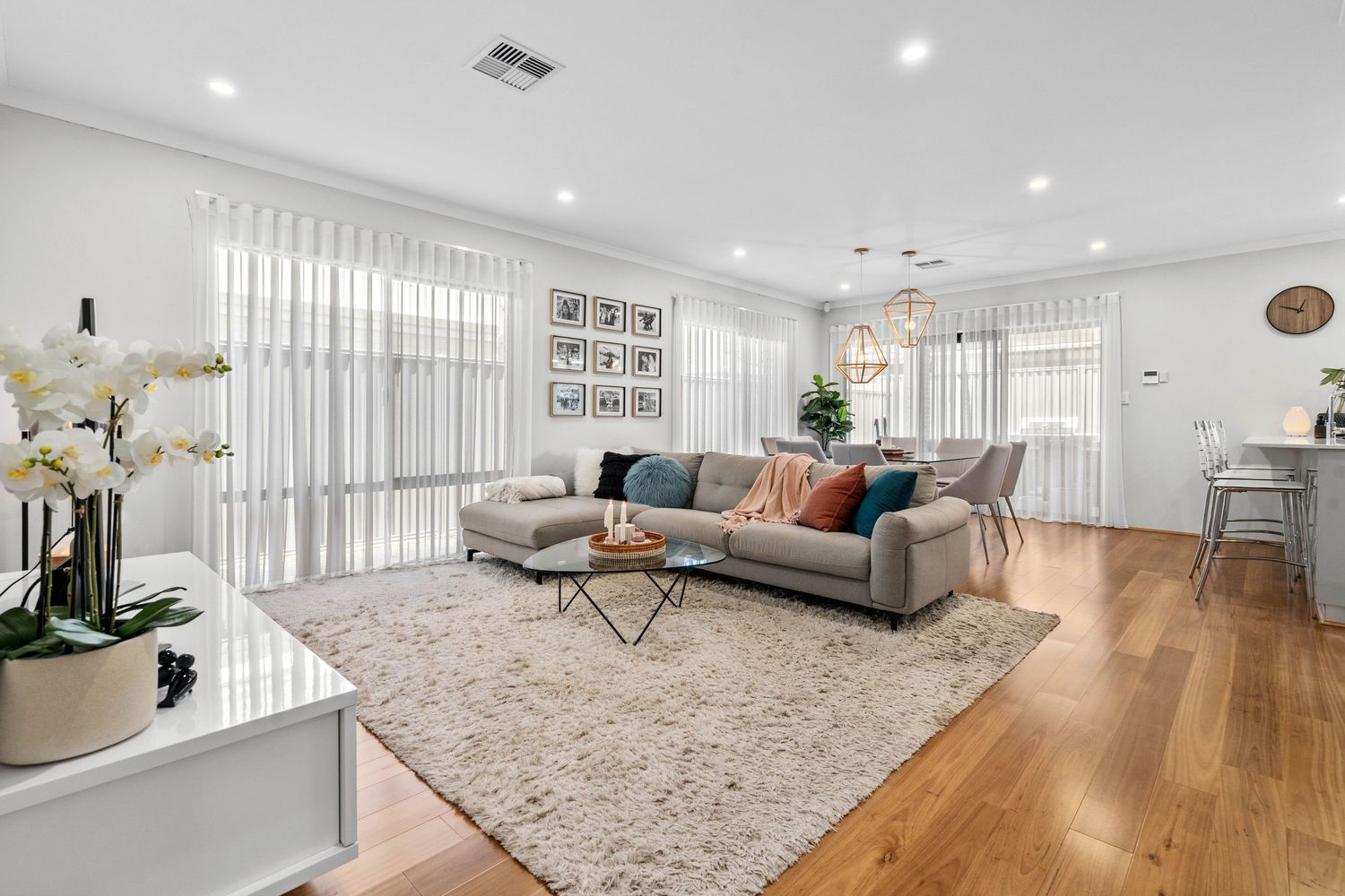 Modern white living room with grey sectional sofa, hardwood floors, and sheer curtains showcasing contemporary decor.