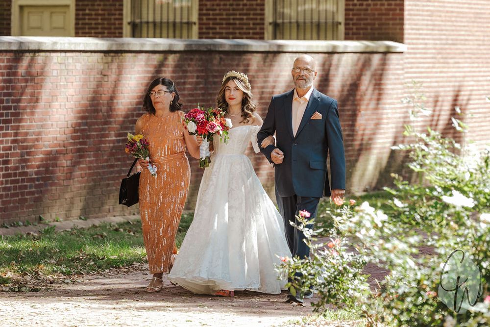 A wedding party walks together along a brick path on a sunny day, with beautiful floral bouquets and formal attire.