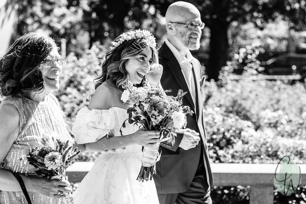 Black and white image of a happy couple smiling while walking in a garden decorated with flowers.