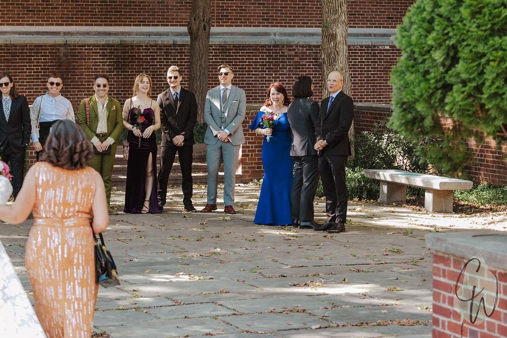 A wedding ceremony taking place outdoors with the bridal party and guests gathered on a brick courtyard.