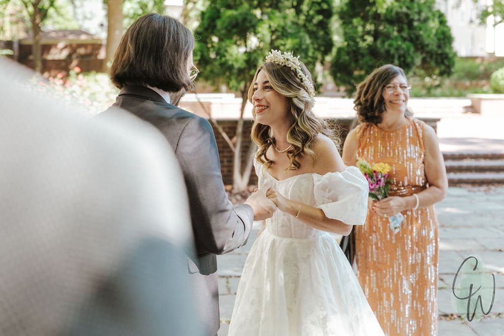 A couple exchanges vows during an intimate outdoor garden wedding ceremony while an officiant presides.