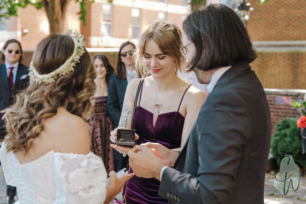 Wedding guests in formal attire gather during outdoor reception as they chat and check their phones.
