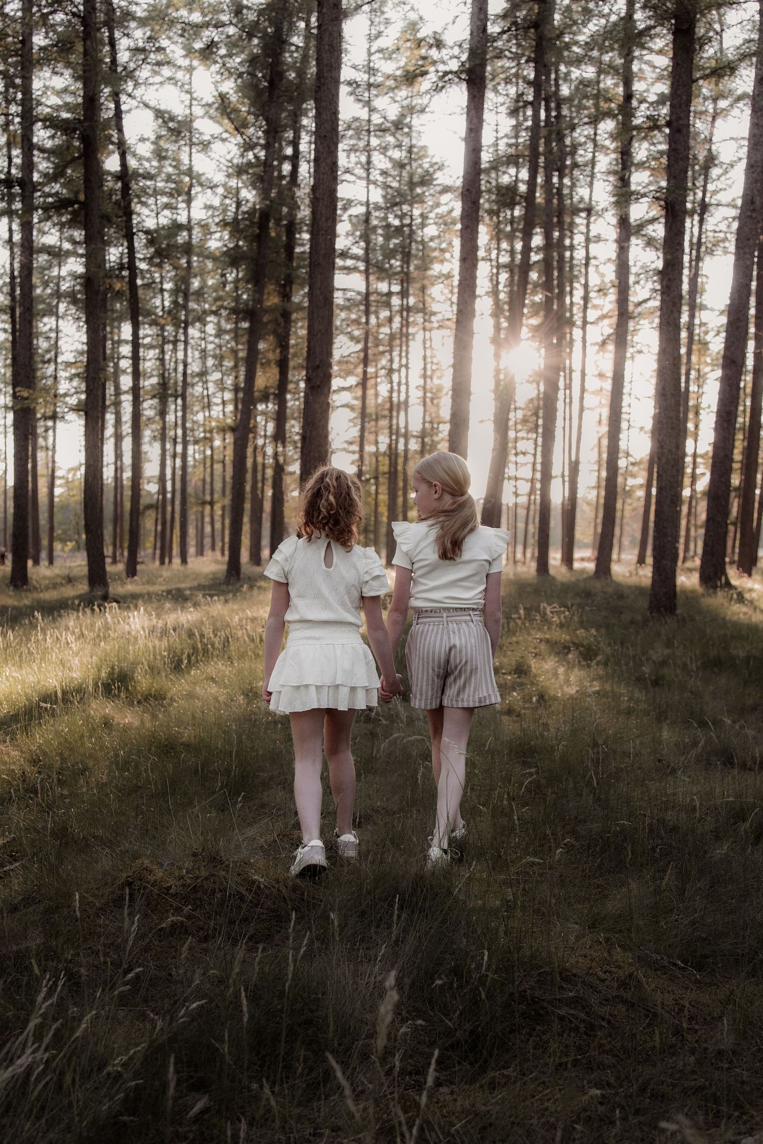 Twee meisjes lopen samen weg in het bos tijdens een fotoshoot in Helmond. Spontane, pure momentopname vol warmte.