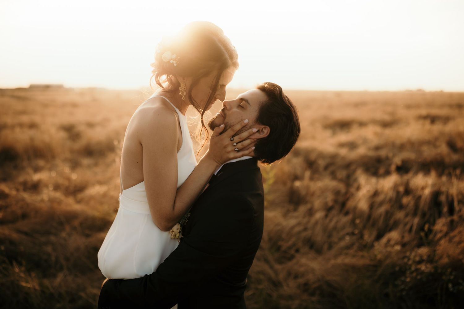Newlyweds embrace passionately in golden field during sunset.