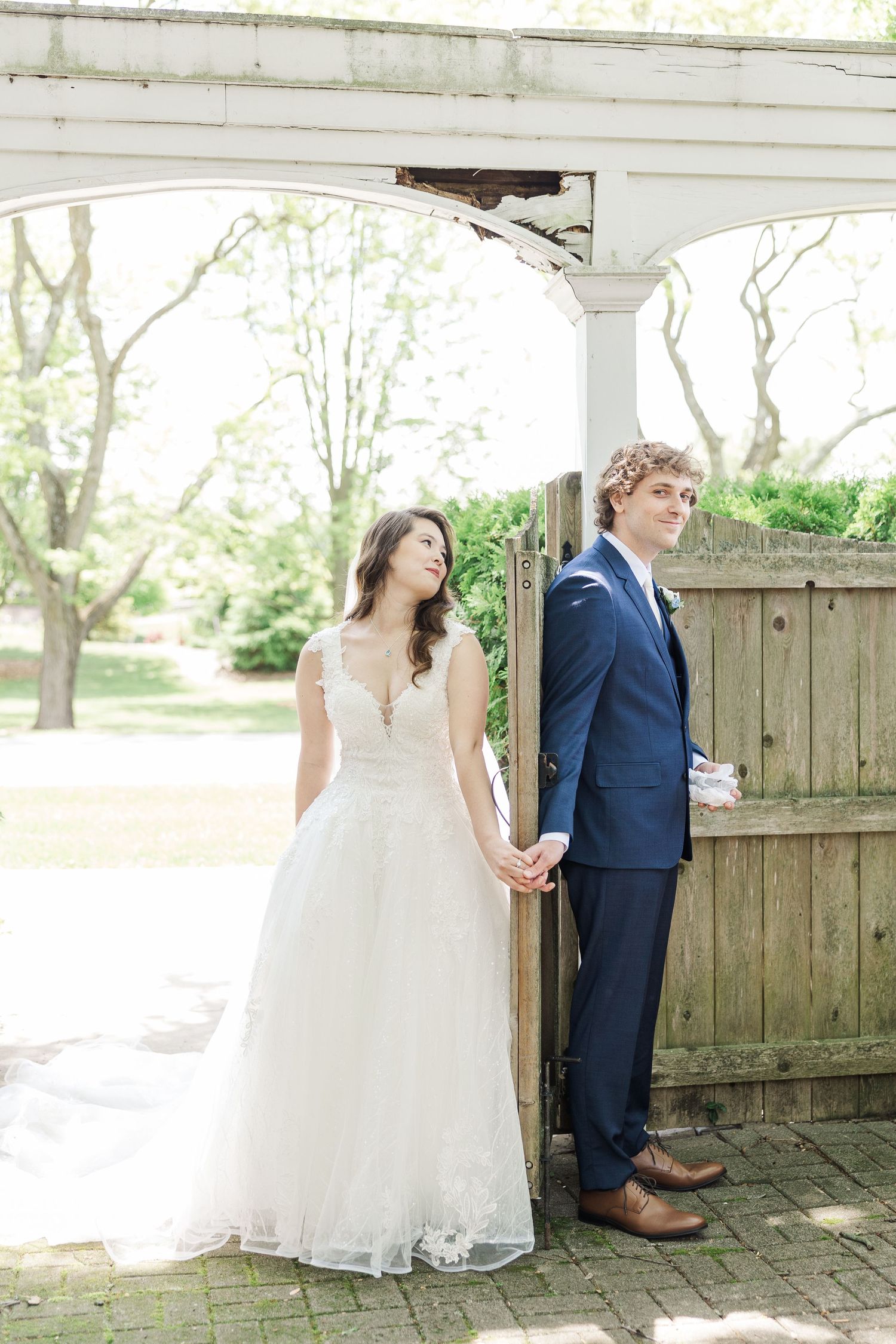 Couple stands on opposite sides of wooden gate during wedding first look photo in romantic outdoor setting.