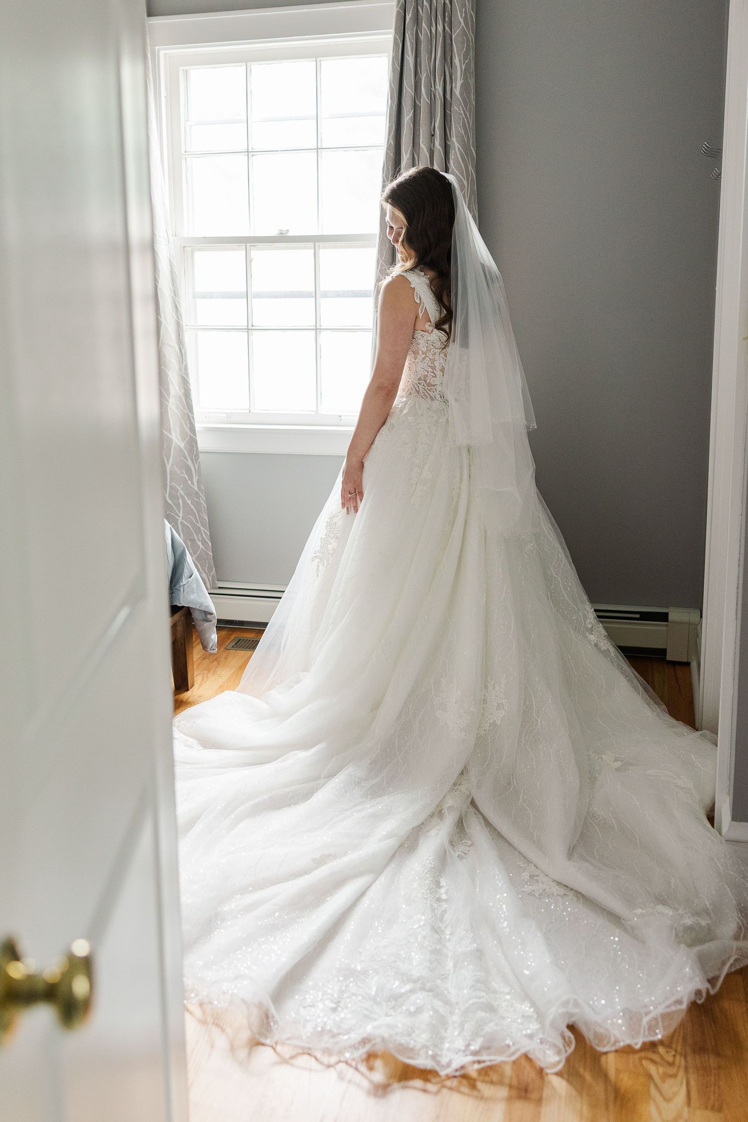 A wedding dress with intricate lace details and flowing train shown from four different angles in a brightly lit room.