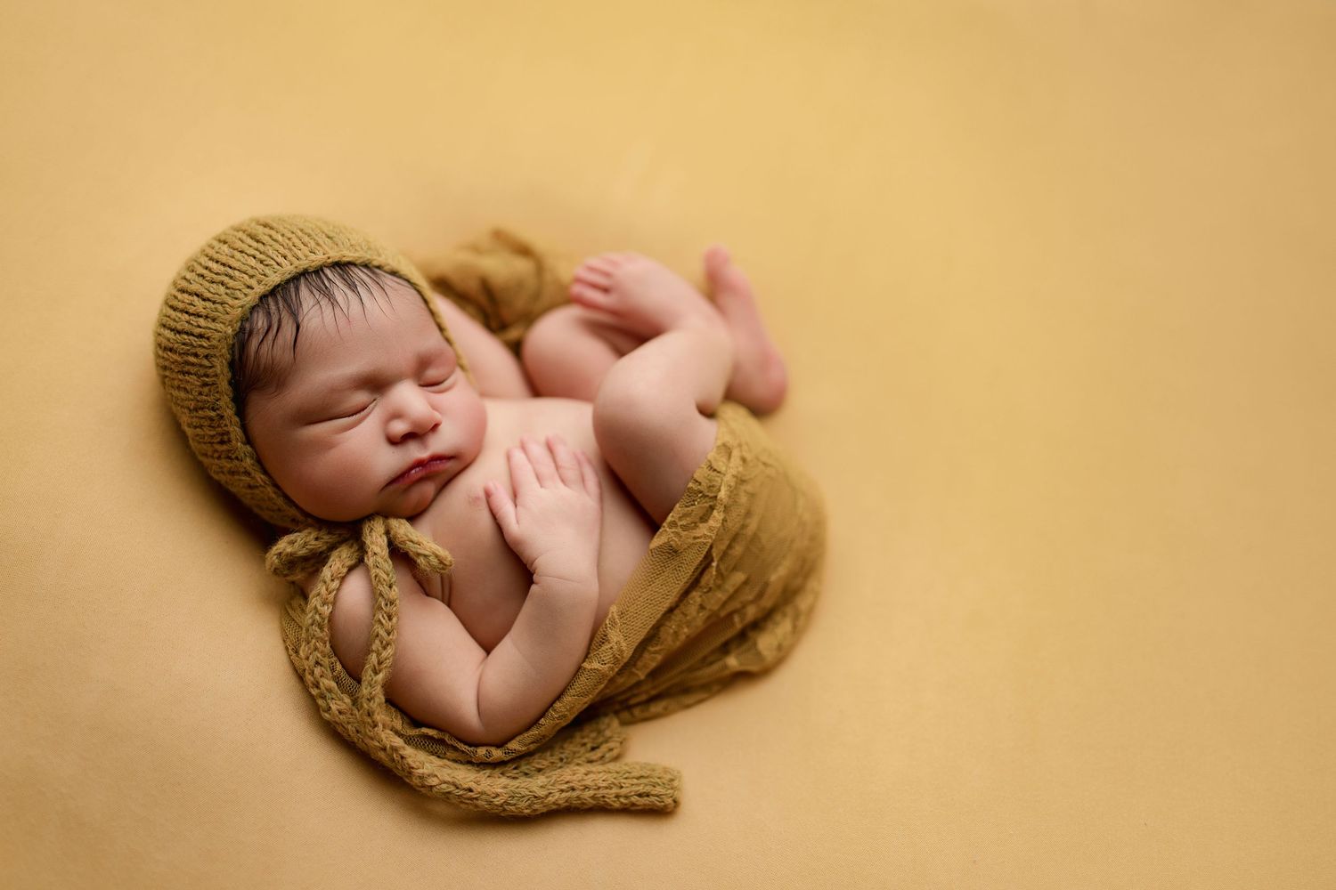 Newborn baby sleeping peacefully wrapped in soft knitted tan blanket on neutral beige background.