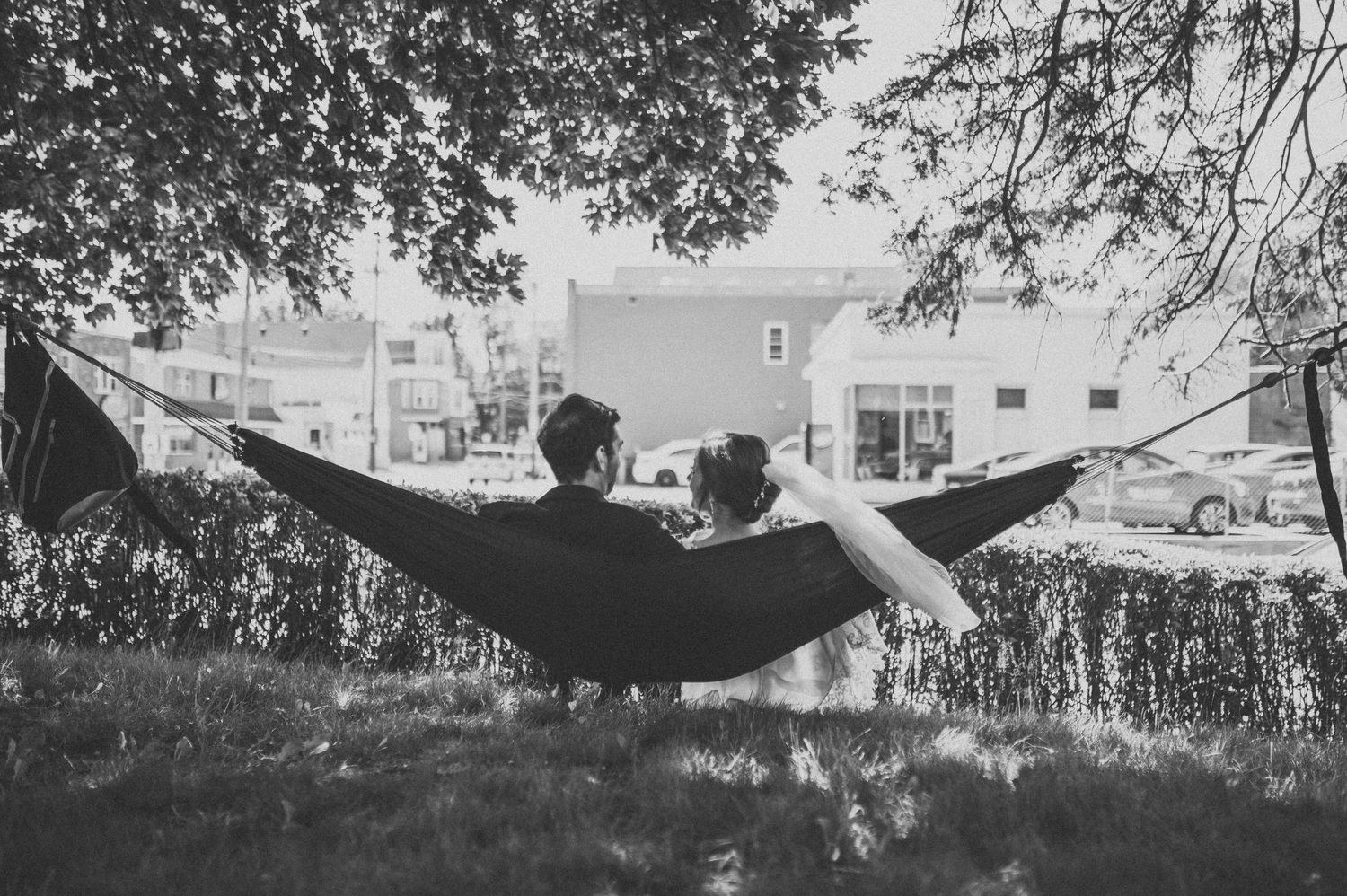 A bride and groom sit in a hammock and glance over at each other in a sweet but romantic portrait of their wedding day.