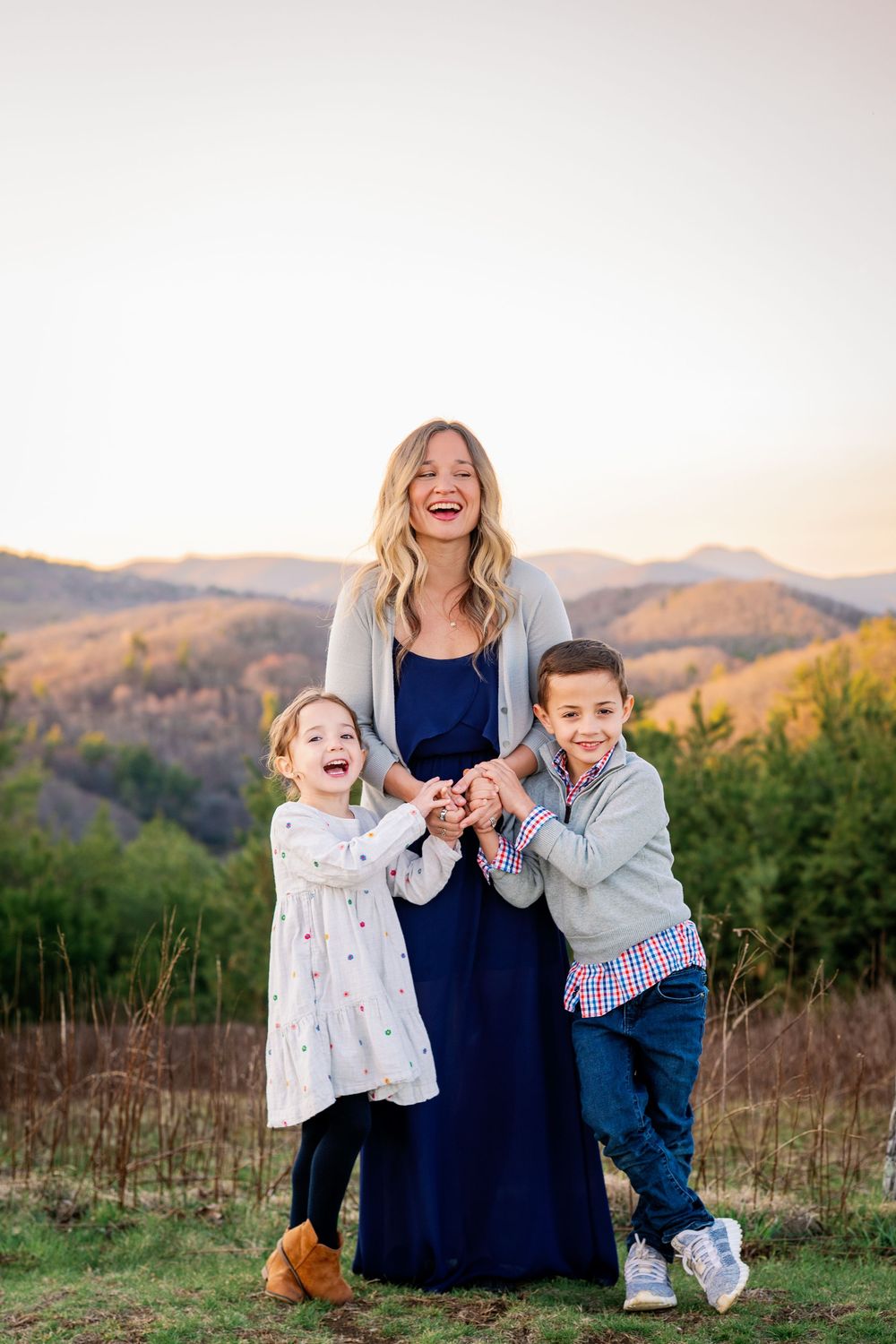 Mother and children sharing a joyful moment together outdoors with rolling hills in the background.