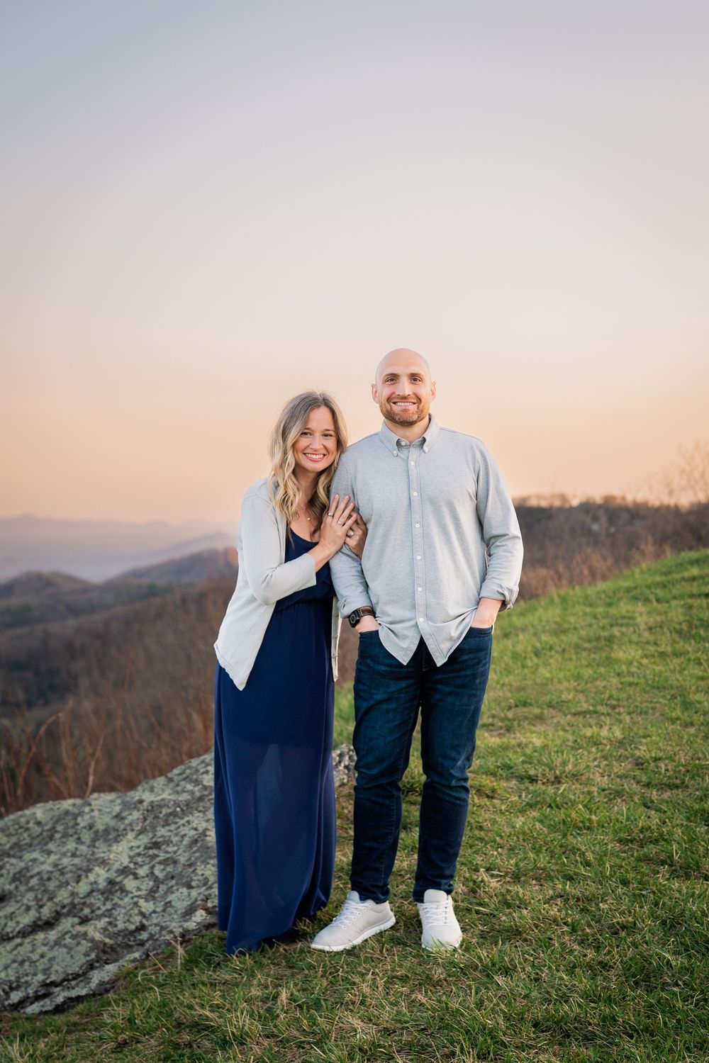 Couple standing together on hilltop with mountain vista in background during golden hour.