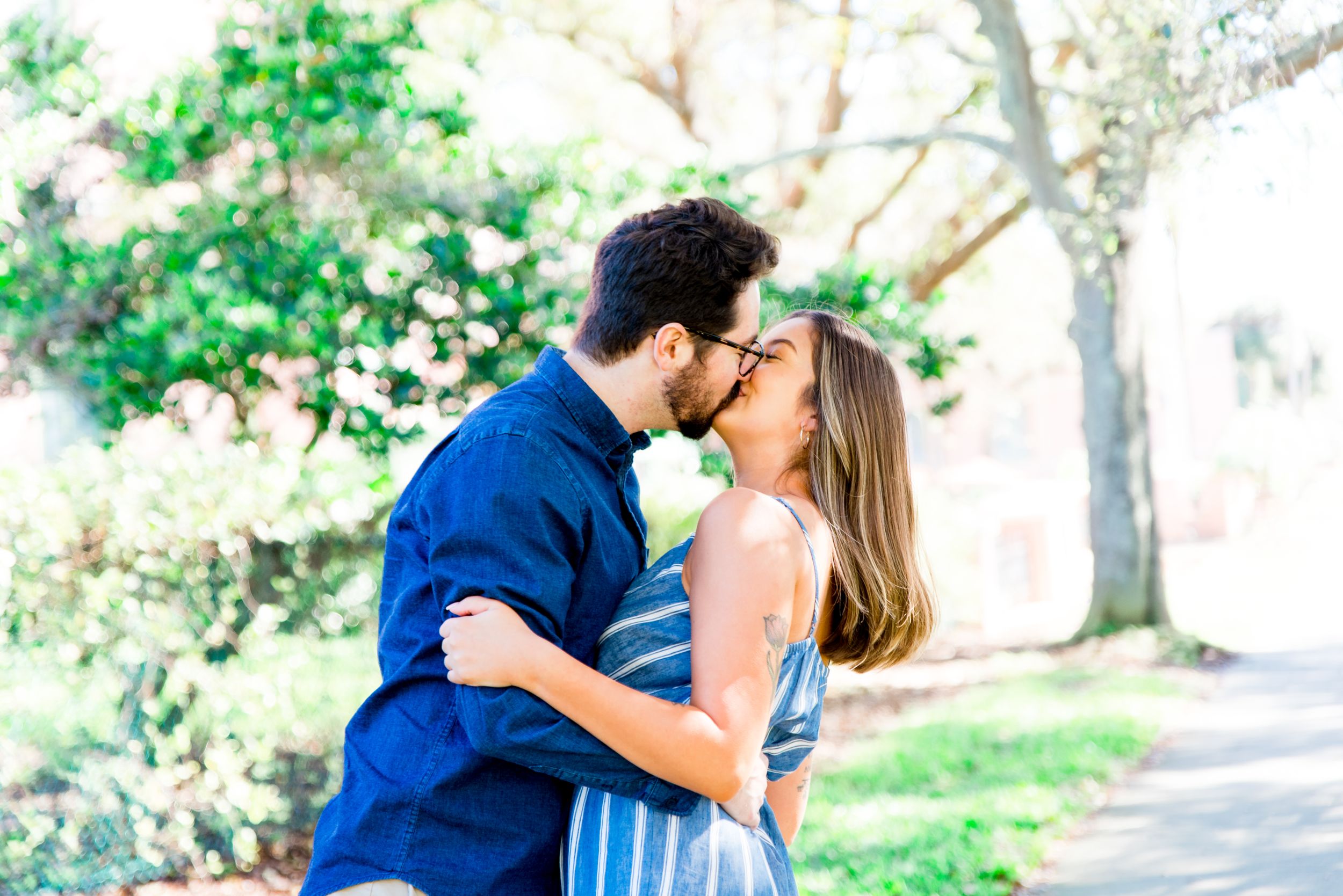 young man in blue shirt kissing woman in blue jumper under trees at St. pete engagement photos in Vinoy Park