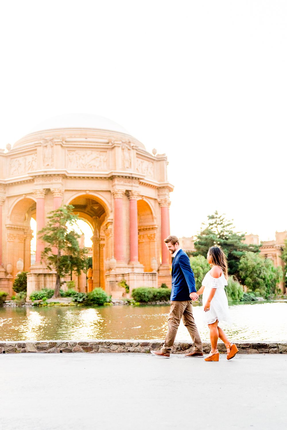 man in blue suit leading woman in white dress in front of Palace of Fine Arts San Francisco engagement pictures