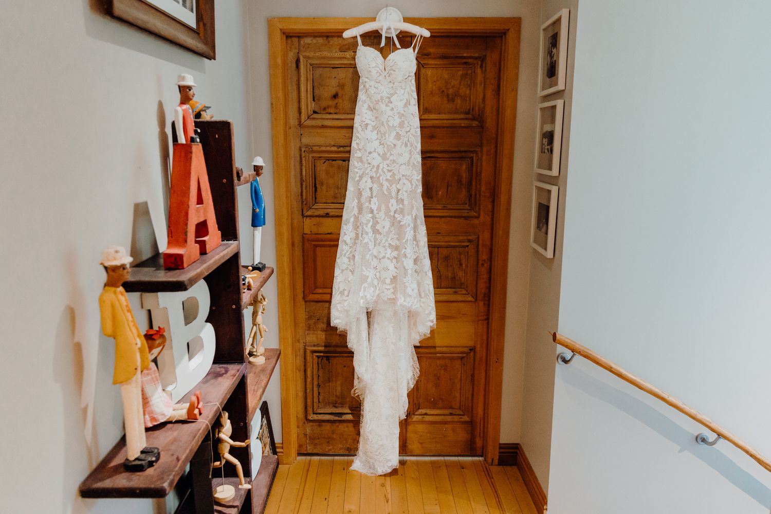 Elegant white lace wedding dress hanging on wooden door in hallway.