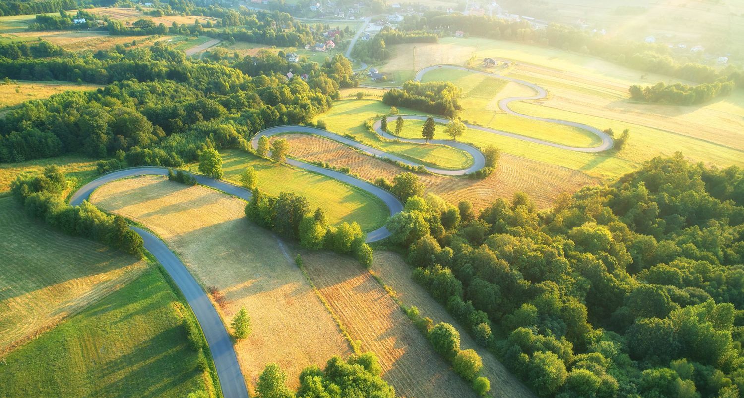 Aerial view of winding river cutting through golden farmland and forest at sunset.