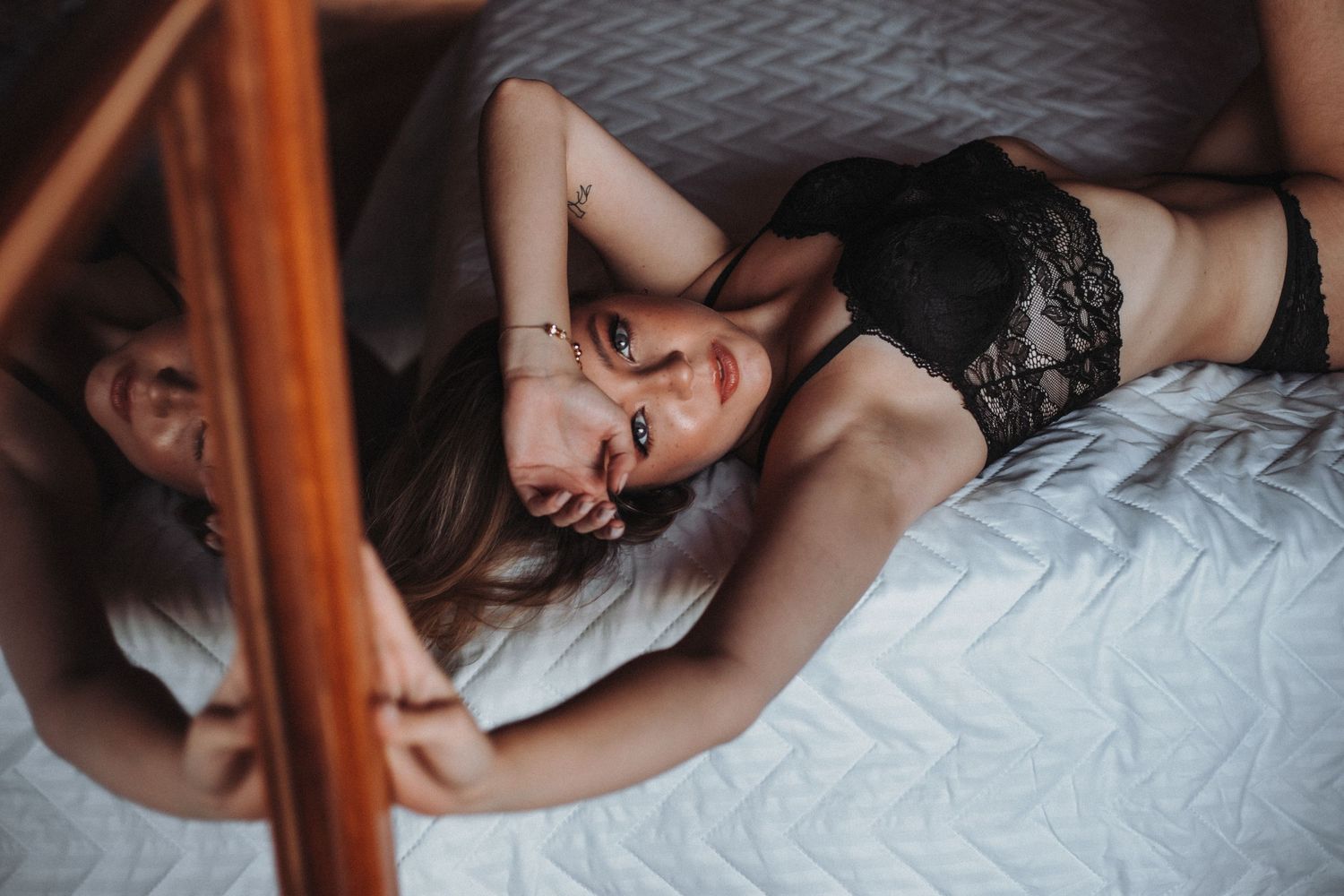 Woman in black lace reflected in mirror while lying on bed.