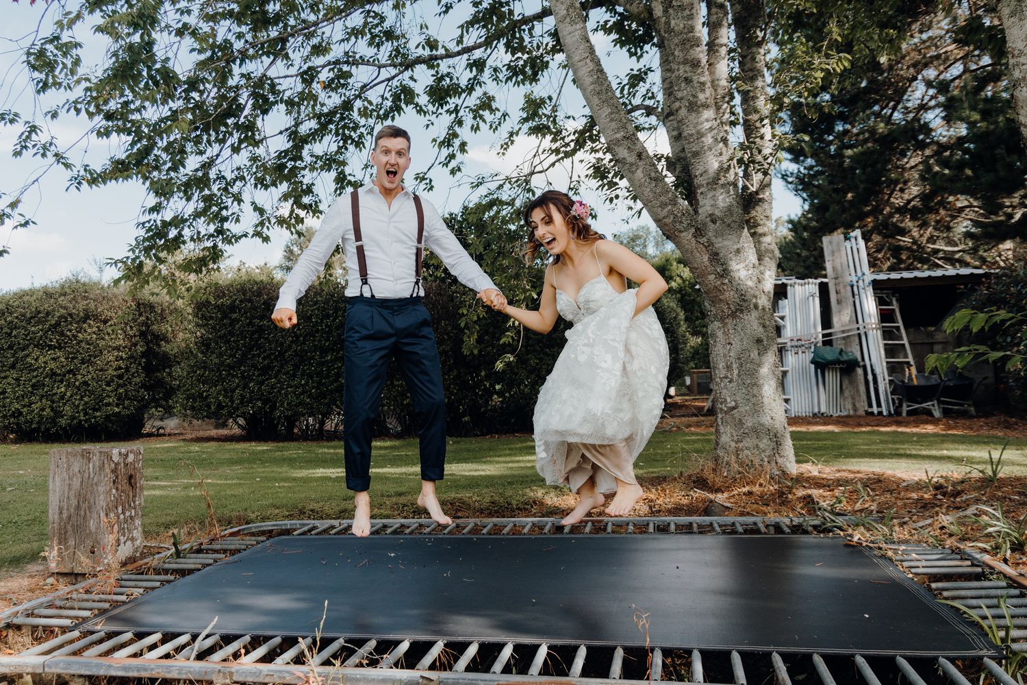 A joyful couple jumping together on a large backyard trampoline.