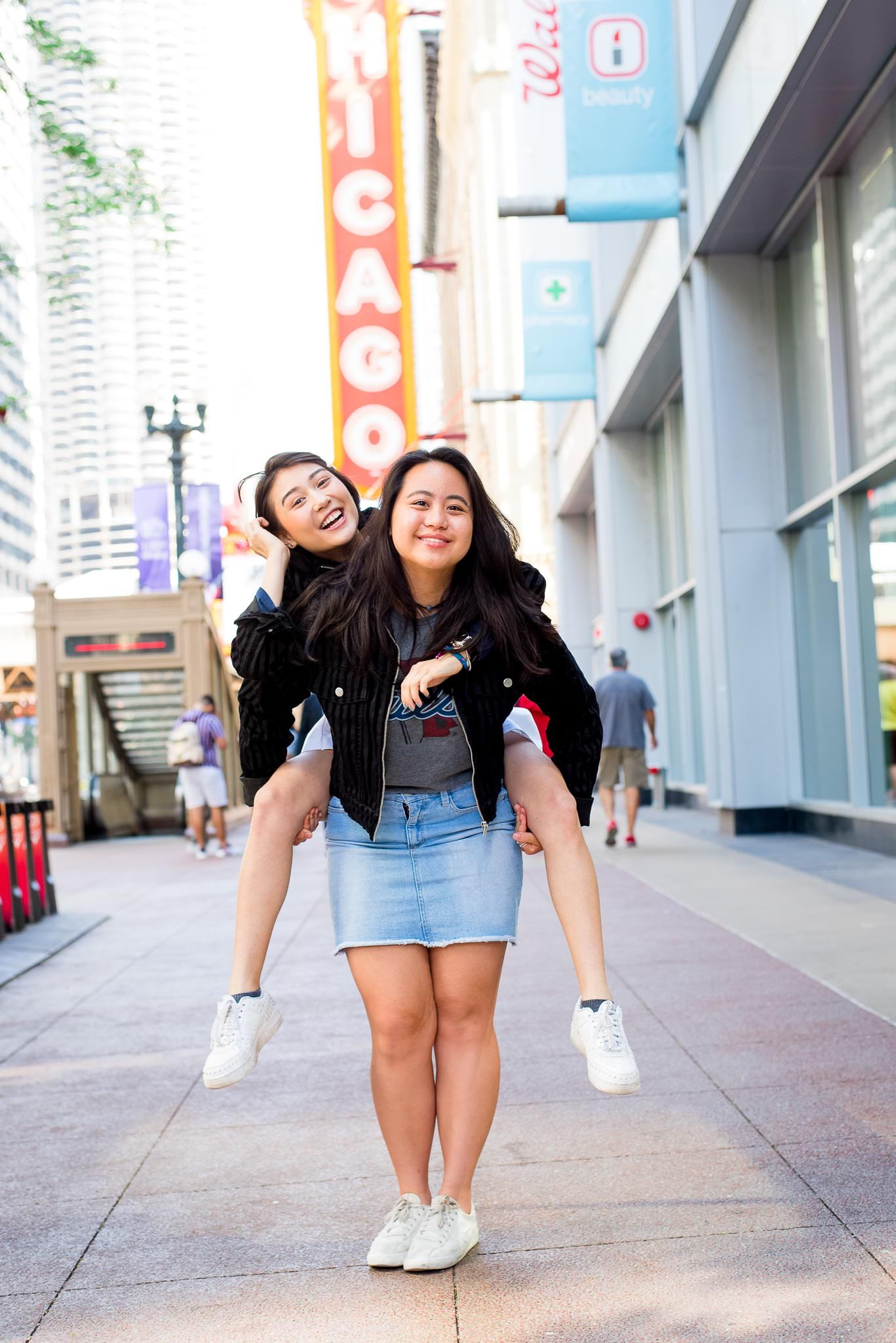 two senior girls in front of the Chicago Theater sign for Chicago senior pictures doing piggyback ride