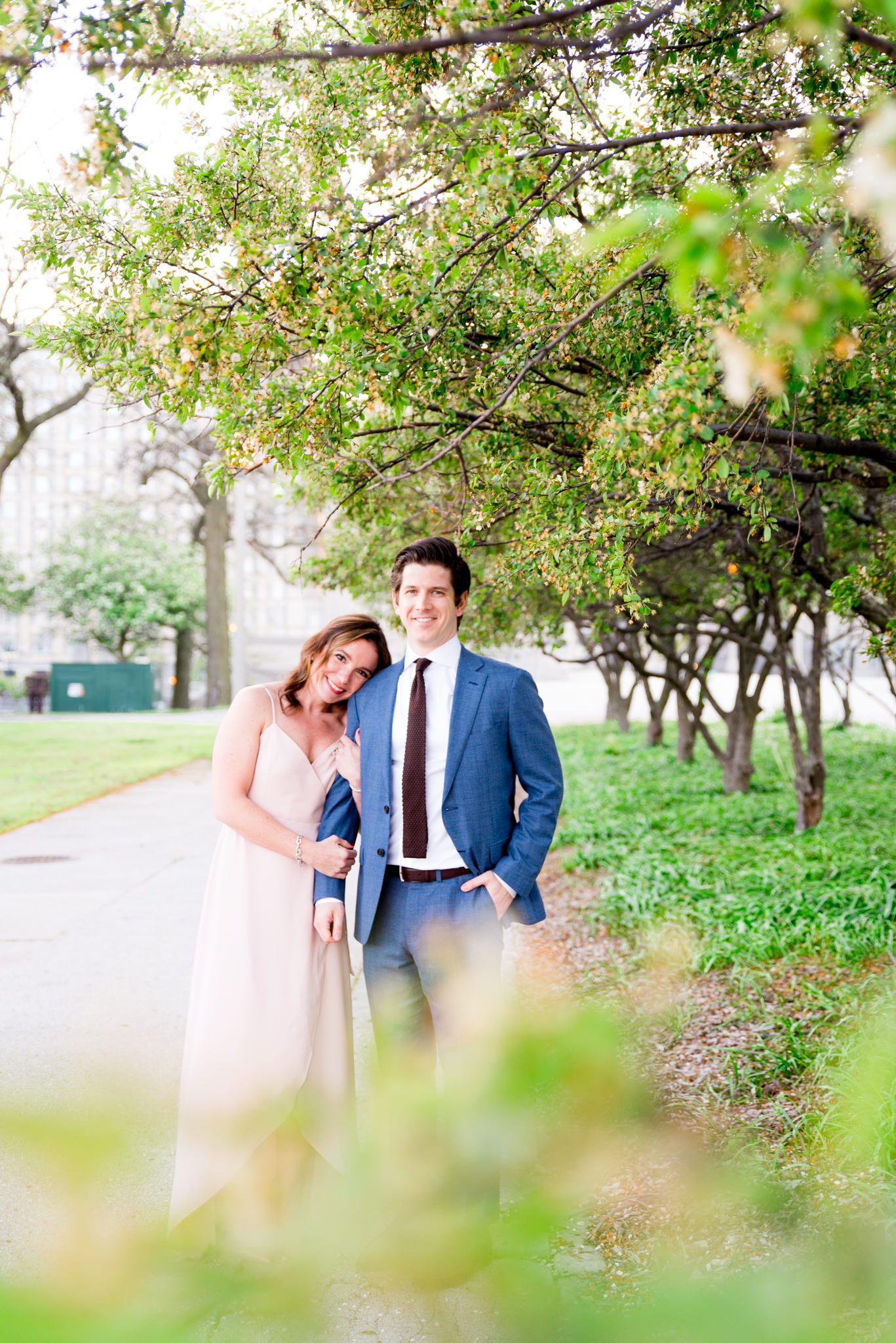 woman in pink dress holding man's arm in navy suit and smiles in Millennium Park in downtown Chicago