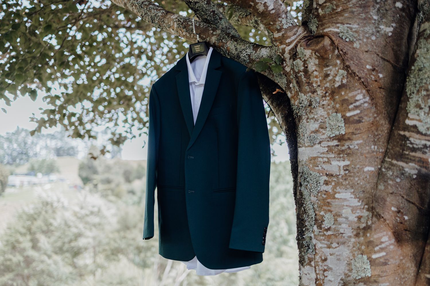 Navy blue suit jacket hanging on tree branch outdoors.