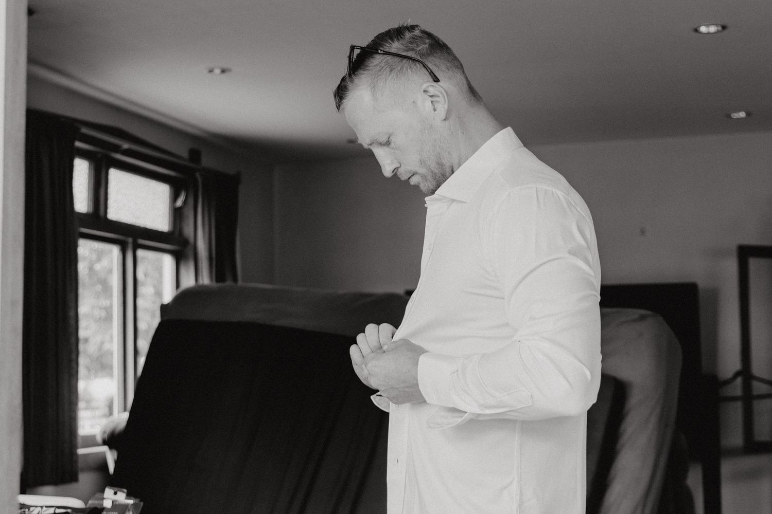 Person in white dress shirt buttoning up while getting ready indoors.