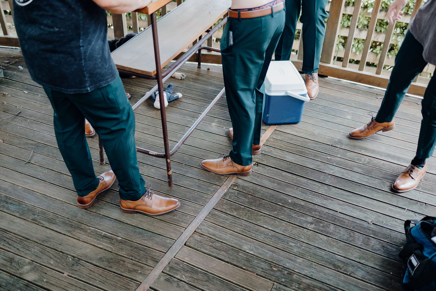 Dress shoes and casual attire on wooden deck during outdoor event.