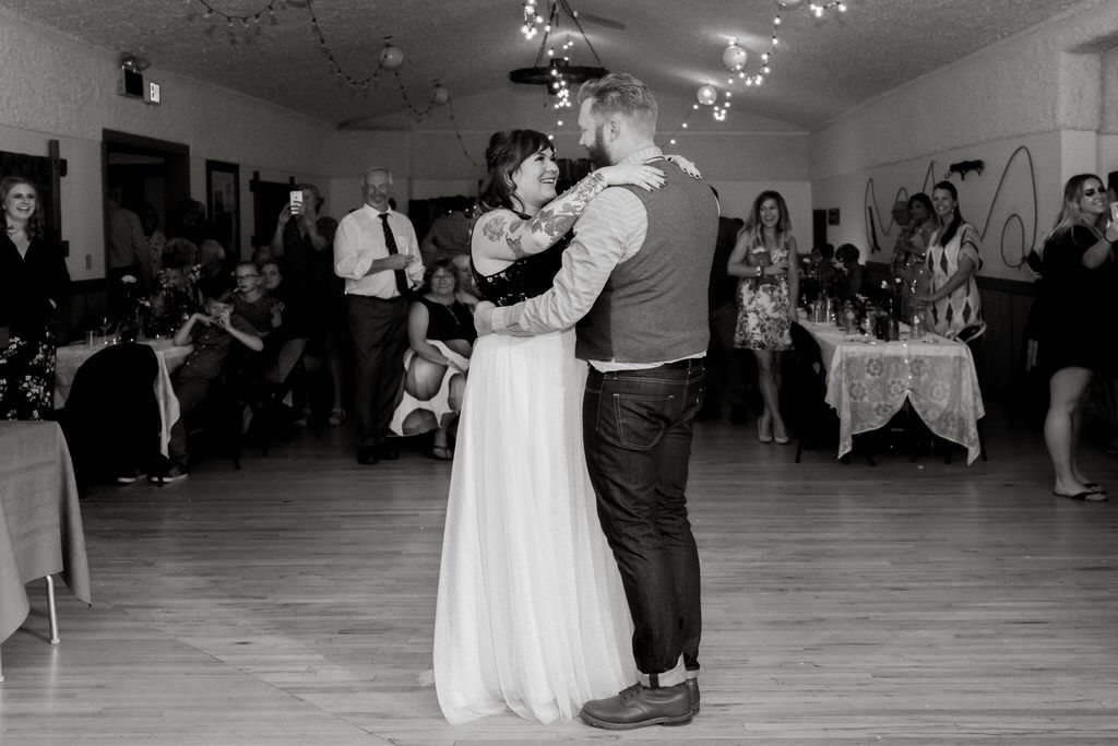 A couple dancing together in a reception hall with guests watching in the background.