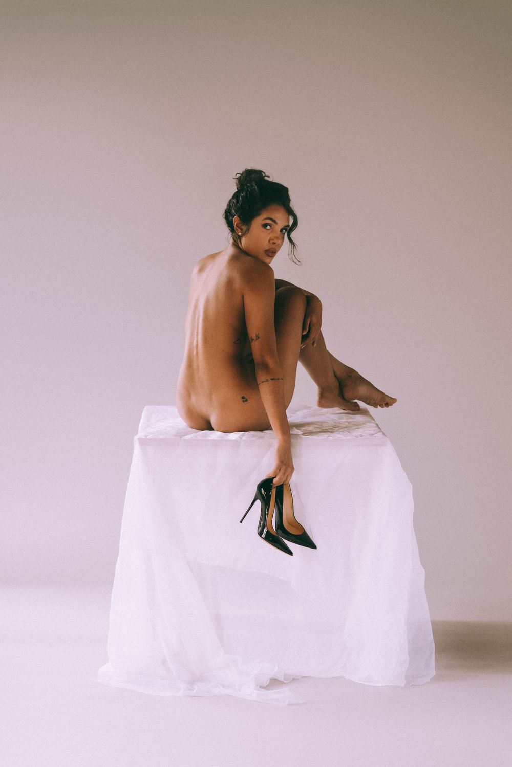 Minimalist artistic nude portrait on white pedestal with black heels.